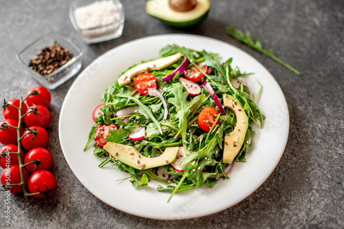 Vegan food. Healthy fresh vegetable salad - tomatoes, arugula, avocado, radish on a stone background. Diet menu.