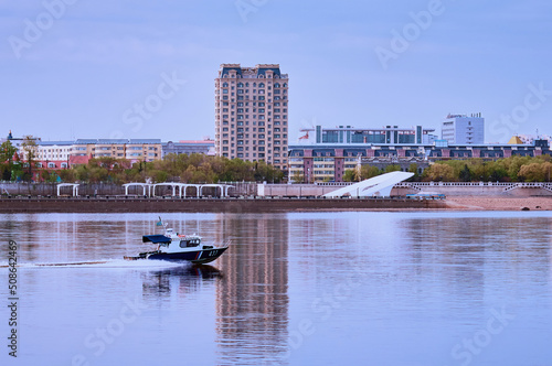 A speedboat of the coast guard of the Russian Federation moves along the smooth surface of the border river Amur. Morning city of Heihe  China in the background. Embankment panorama.