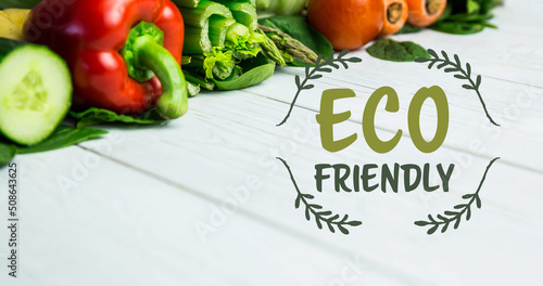 Image of eco friendly text in green over fresh organic vegetables on wooden boards