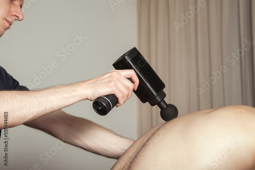 Gun percussion massage back muscle athletic man in medical room