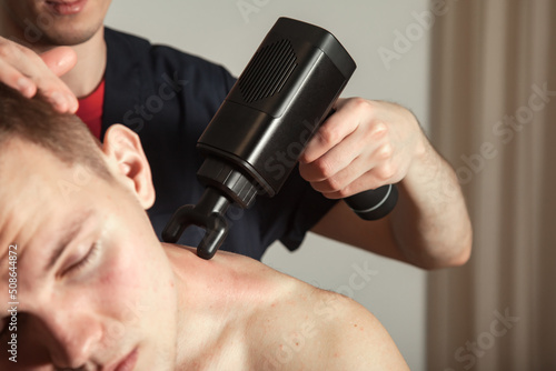 Neck gun percussion massage muscle athletic man in medical room