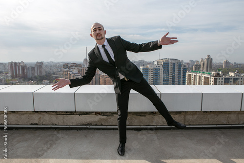 a man in a black suit with a tie stands on the roof against the backdrop of the panorama of the city