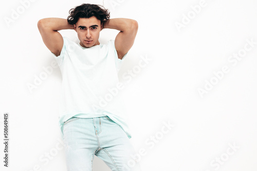 Portrait of handsome confident stylish hipster lambersexual model.Man dressed in over size T-shirt and jeans. Fashion male isolated in studio. Posing near white wall