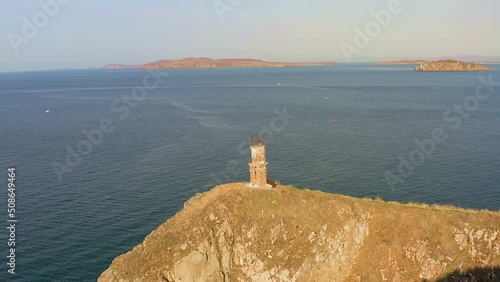 Beautiful high vertical cliffs at dawn. Abandoned lighthouse on top of the rocks. Untouched nature. Drone view. Shkot Island, Vladivostok photo