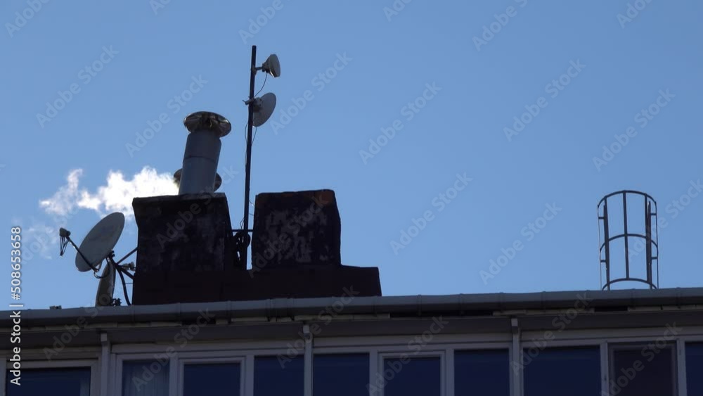 Rooftops with smokey chimneys. Satellite on a rooftop during windy day. Antennas and electromagnetic towers with satellite dish, microwaves antenna at rooftop station of middle class house. Rooftops with smokey chimneys. Satellite on a rooftop during windy day. Antennas and electromagnetic towers with satellite dish, microwaves antenna at rooftop station of middle class house.