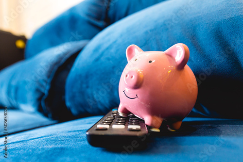 Um cofrinho com um controle remoto como se estivesse vendendo com uma televisão em um sofá azul. Conceitos de televisão por assinatura, economia de dinheiro e finanças do lar. photo