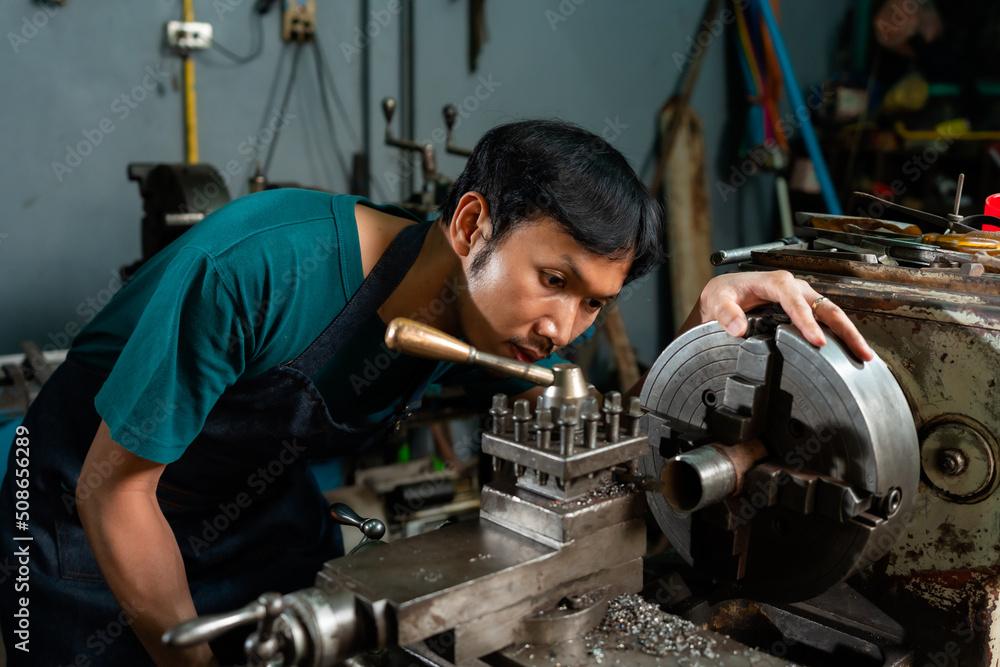 Close-up of the face of the mechanic in a small factory, with a serious expression on the control of the lathe, which he is currently controlling. Close-up of the face of the mechanic in a small factory, with a serious expression on the control of the lathe, which he is currently controlling.