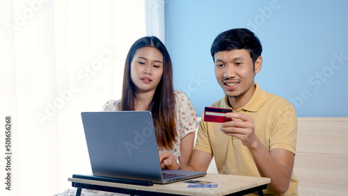 Young Asian man, couple looking at shopping, and ordering online via laptop computer, two people choosing a credit card to pay for their purchases.,online shopping.