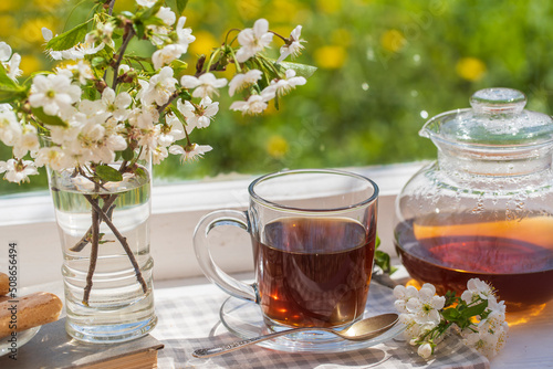 Hot tea in glass teapot and cup on windowsill at home