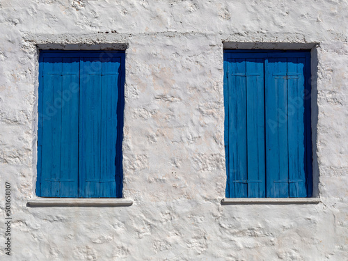 Two windows with closed blue shutters on a white-washed wall  Perdika village  Aegina island  Greece. Space for your text or logo.
