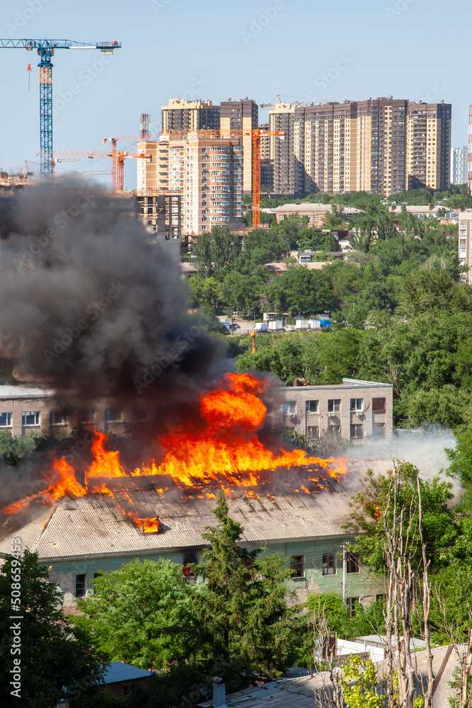 Fototapeta premium Old and new. An old abandoned building is burning against the background of new buildings
