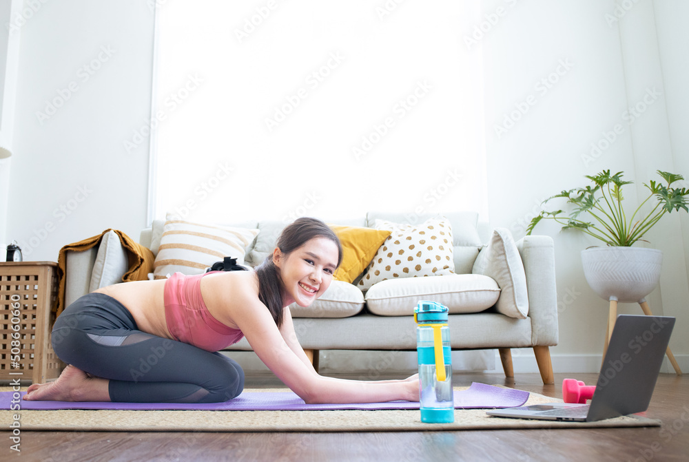 Asian young healthy woman slim strong sexy female sporty model in casual crop top sportswear laying down smiling on carpet floor in living room learning yoga workout class via laptop computer. Asian young healthy woman slim strong sexy female sporty model in casual crop top sportswear laying down smiling on carpet floor in living room learning yoga workout class via laptop computer.