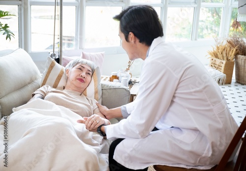 Asian Doctor Talking With Senior Female Patient In Bed At Home.Paliative care for Elder woman at home.Elderly senior patient (Asian old aging person) in nursing hospice holding geriatrician doctor.