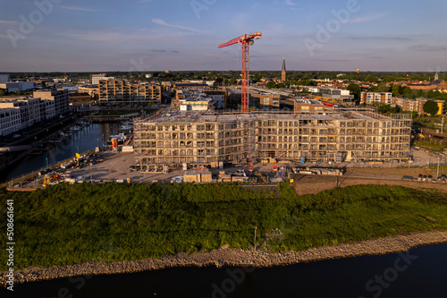 Aerial view of scaffolding luxury Kade Zuid apartment complex construction at riverbank of river IJssel between train tracks and recreational port. 