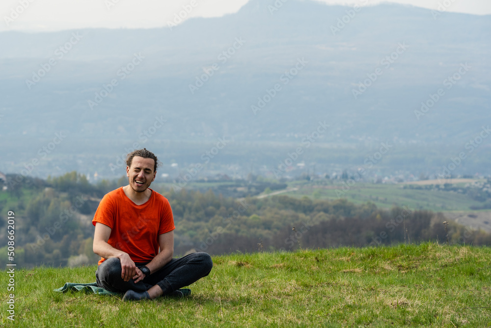 Young smiling man sitting on the mountain peak