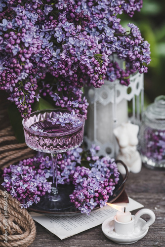 A candle and fancy glasses for dessert and champagne with a lilac drink and lilac flowers inside. The fashionable shade of 2022 is very relevant. The concept of a party and a holiday. Still-life.