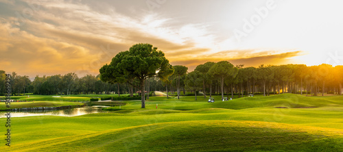 Golf course at sunset with beautiful sky. Scenic panoramic view of golf fairway. Golf field with pines
