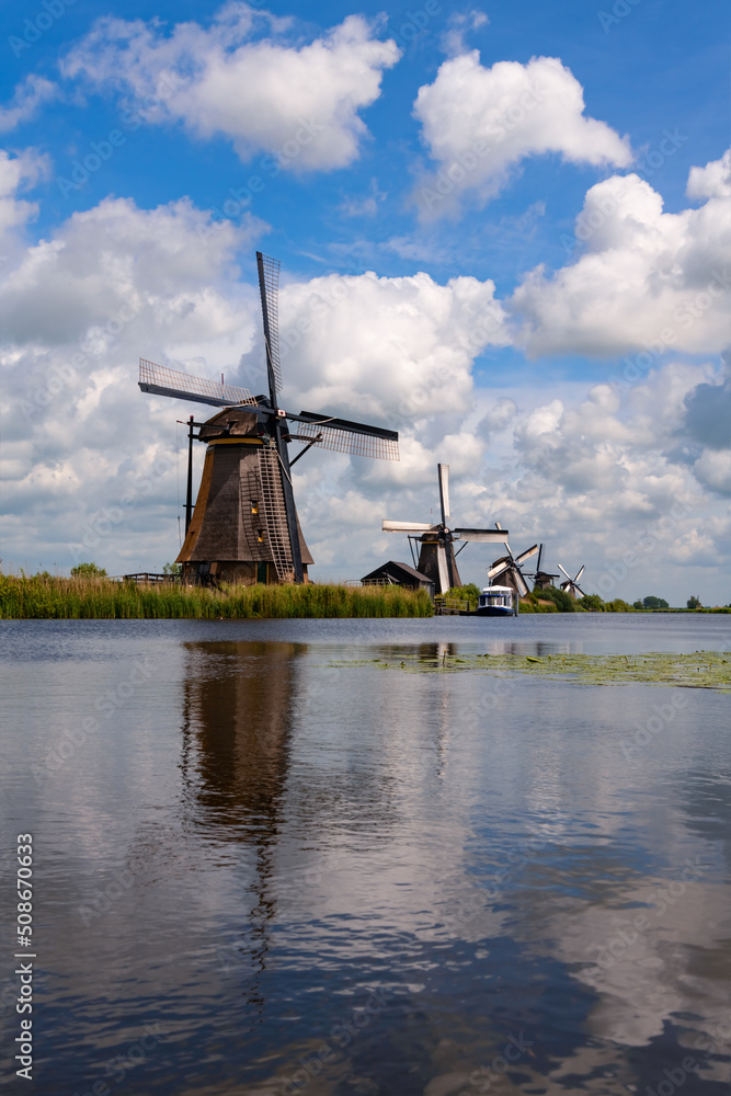 Row of windmills in “Kinderdijk“, popular Dutch tourist site and world heritage spot. Historic renovated wind water pumps for drainage in Alblasserwaard polder, Netherlands on a sunny day with clouds.