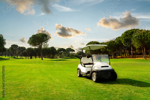 Golf cart in fairway of golf course with green grass field with cloudy sky and trees at sunset in Belek, Turkey photo