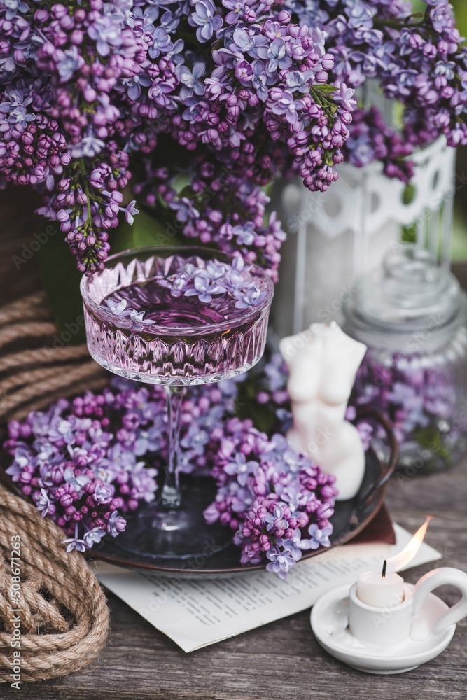 Obraz premium A candle and fancy glasses for dessert and champagne with a lilac drink and lilac flowers inside. The fashionable shade of 2022 is very relevant. The concept of a party and a holiday. Still-life.