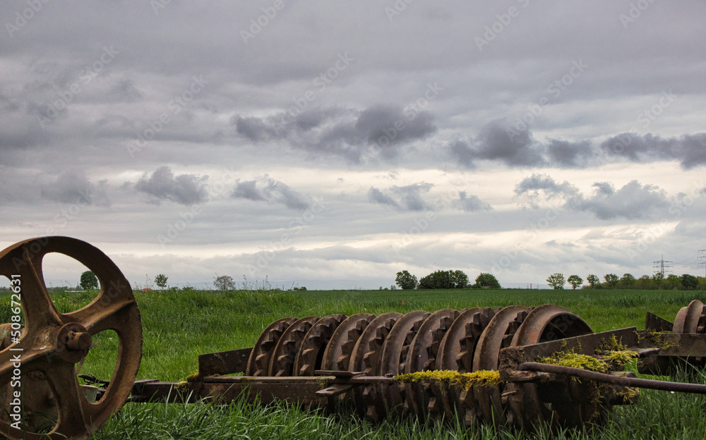Ein rostiges Landwirtschaftsgerät liegt einsam und verlassen auf einem Acker und symbolisiert den Frühling Ein rostiges Landwirtschaftsgerät liegt einsam und verlassen auf einem Acker und symbolisiert den Frühling
