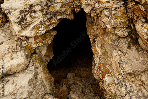The concept of the cave people's habitat. A stone wall with a dark hole, the entrance to the cave. The habitat of wild animals. Close-up