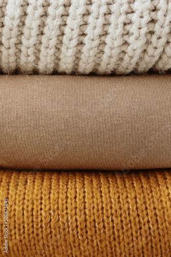 Stack of knitted wool sweaters, different knitting patterns sweaters folded in stack. sofa