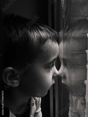 black and white portrait of a little boy who looks out the window, sealed with scotch tape, in order to protect from the blast wave during the war in Ukraine