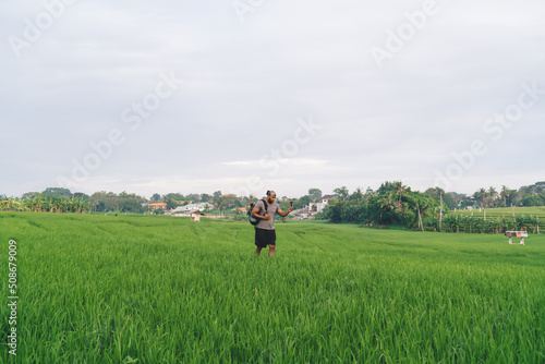 Millennial man with touristic backpack shooting influence content via modern gopro technology, casual dressed hipster guy exploring rice fields and photographing scenic views via waterproof camera