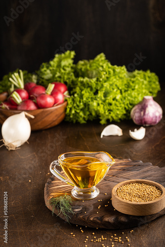 Mustard oil on wooden board background with fresh vegetables. Vertical