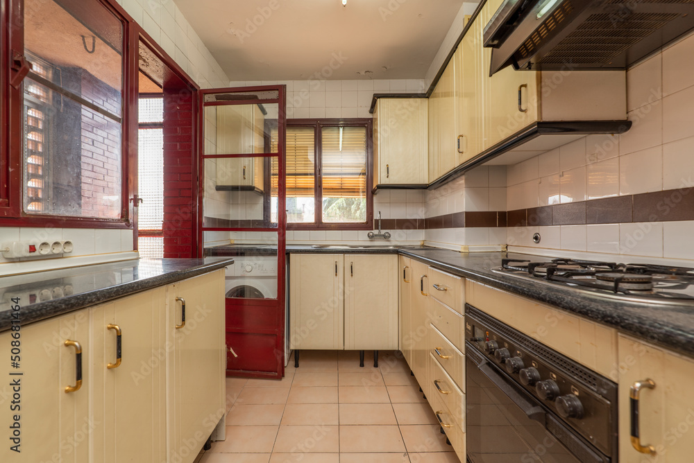Fototapeta premium Kitchen with black countertops cream cabinets gas burners and some red windows and a door that leads to a drying deck