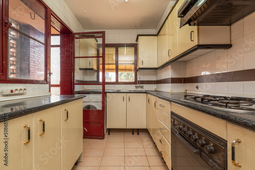 Kitchen with black countertops cream cabinets gas burners and some red windows and a door that leads to a drying deck