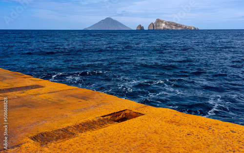 Liparische Inseln, die besondere Insel PANAREA: der Hafen mit rostigem Kai und dem blauen Meer, im Hintergrund Stromboli