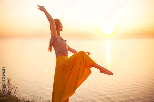 Young woman engaged in yoga in nature with view and warm light of sunset, makes poses enjoy the meditation, balance and sunrise