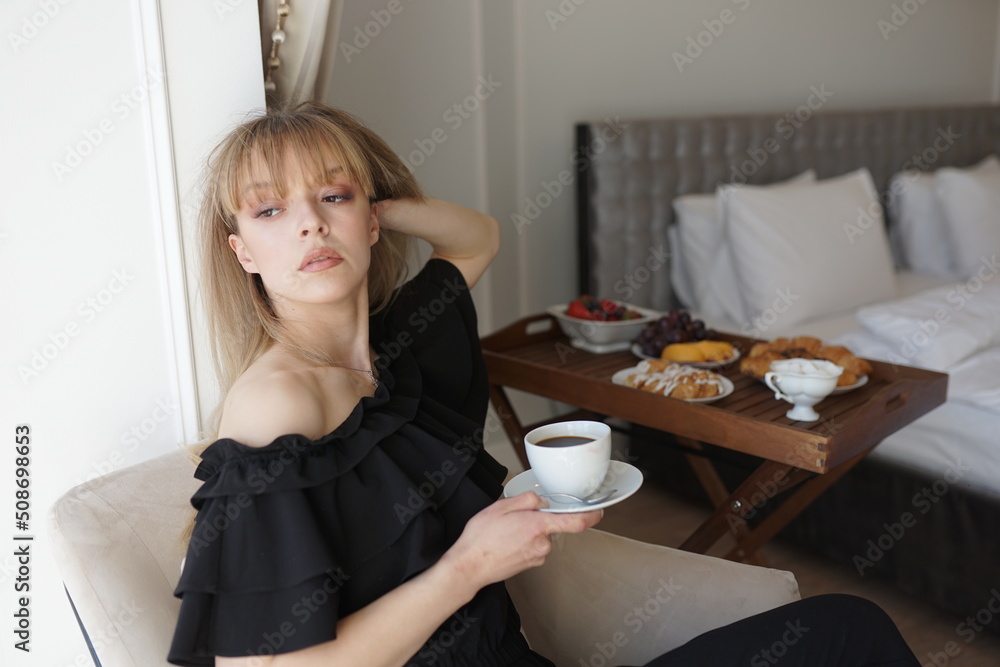 In the photo, the girl is drinking coffee at her balcony. A man takes a picture of her, she is enjoying the morning and breakfast In the photo, the girl is drinking coffee at her balcony. A man takes a picture of her, she is enjoying the morning and breakfast