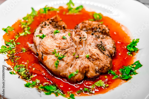 Slice of homemade dogfish dish in red sauce with parsley and herbs in a white plate. Overhead Macro Close-up photography with shallow depth of field, selected focus on the middle of the medallion.