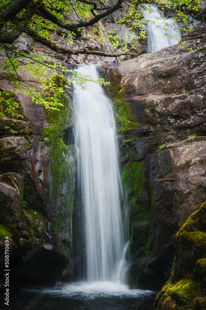 Cascades of a scenic waterfall framed by tree foliage and red cliffs covered by green moss Cascades of a scenic waterfall framed by tree foliage and red cliffs covered by green moss