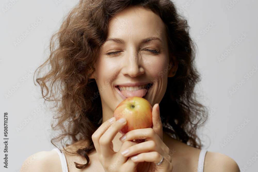 Funny cute curly beautiful woman in basic white t-shirt enjoy licks fresh apple healthy food posing isolated on over white background. Natural Eco-friendly products concept. Copy space Funny cute curly beautiful woman in basic white t-shirt enjoy licks fresh apple healthy food posing isolated on over white background. Natural Eco-friendly products concept. Copy space