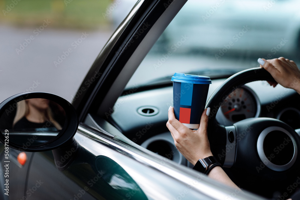 cropped photo of woman's hand holding blue paper cup of coffee in car. Hot drink take away. Travel with coffee. Concept of coffee with you. Mockup