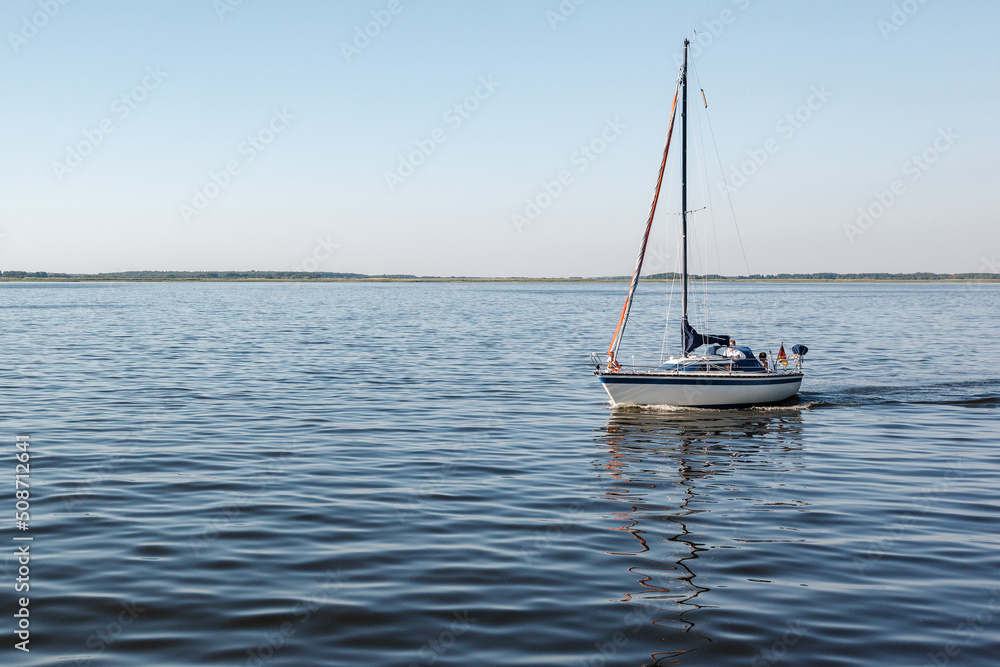A quiet summer day and a lonely yacht with lowered sails and the German flag in the lagoon.