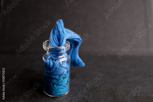 frasco de vidrio pequeño sobre fondo de madera negra con textura que simula agua saliendo pero con madeja de hilos de algodón color azul