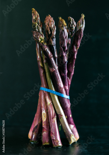 Purple Asparagus on black background with a blue rubber band. 