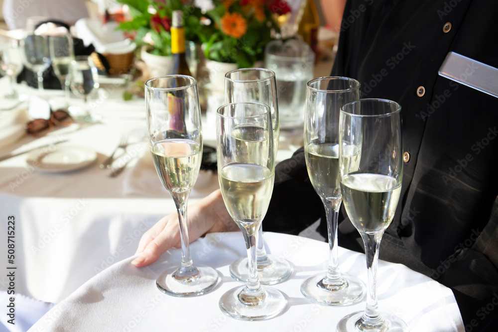 Fototapeta premium waiter in black clothing holding tray cover in white cloth. Four champagne glasses with light champagne inside