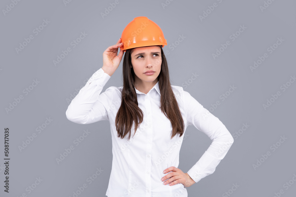 Funny woman in helmet on gray background. Architect businesswoman in helmet thinking, young caucasian female in work as constructor engineer. Funny woman in helmet on gray background. Architect businesswoman in helmet thinking, young caucasian female in work as constructor engineer.
