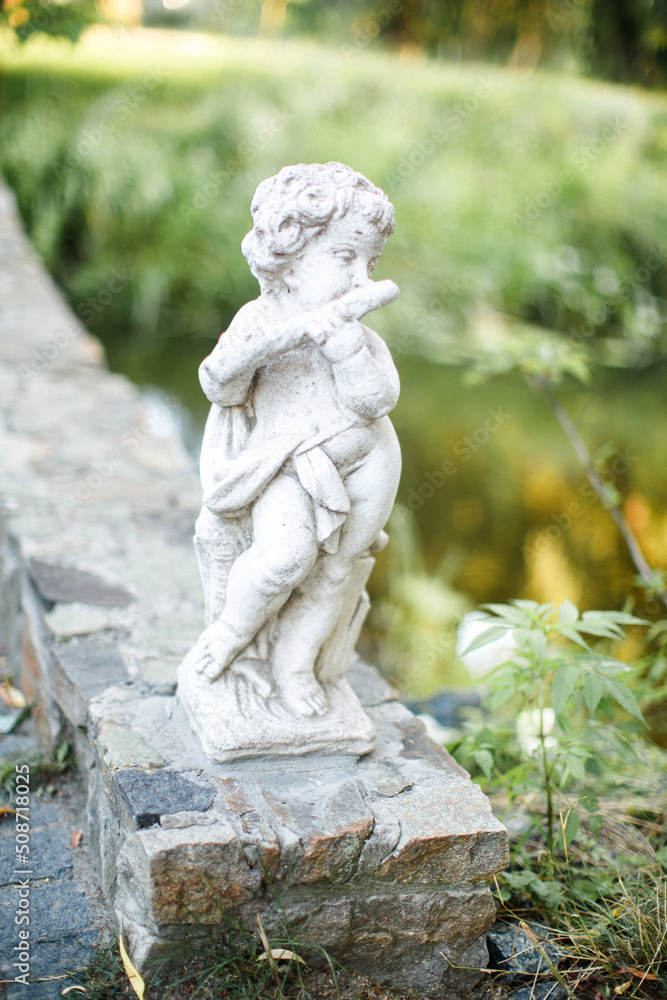 The cute stone statue playing flute instrument in the garden. Angel sculpture