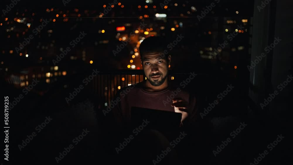 Young African AMerican man sitting on balcony with urban view and using tablet at night Young African AMerican man sitting on balcony with urban view and using tablet at night