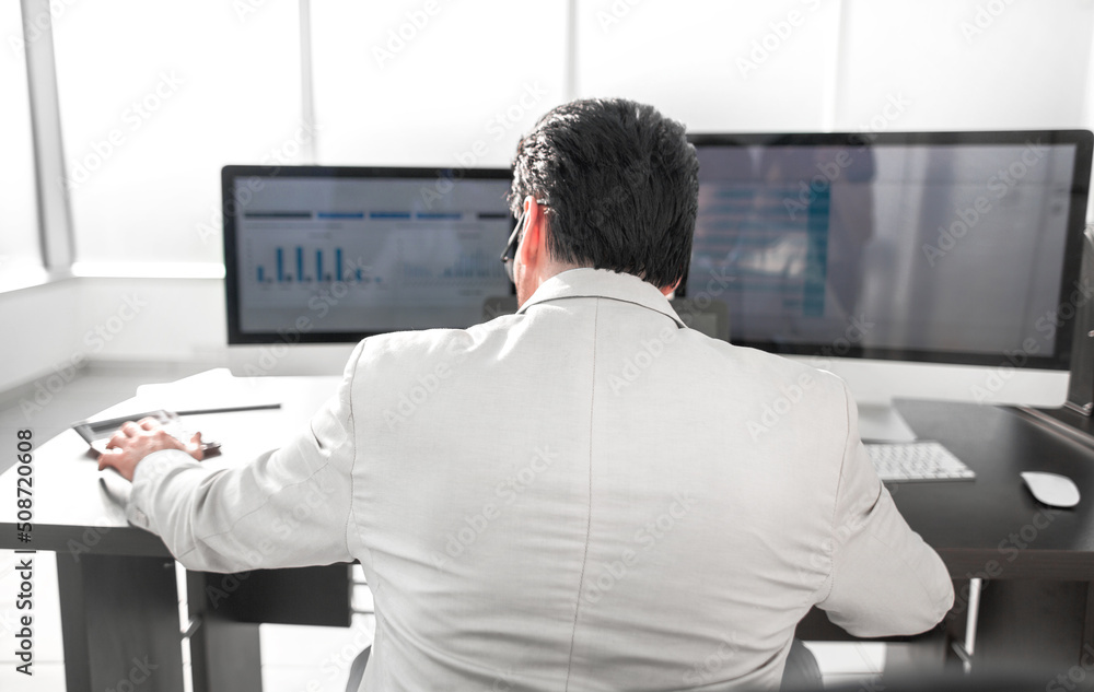 rear view. businessman analyzing graphs on computer