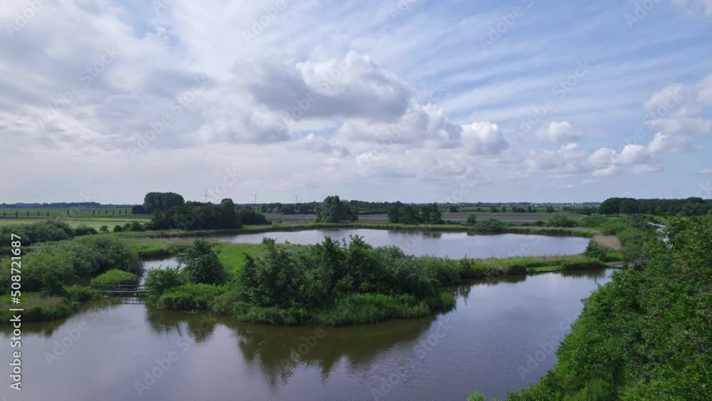 Dutch countryside, with farmland and fresh green nature. Drone flies low over the treetops and over the pond with swampy islands and reeds and shrubs. Beautiful blue sky and white clouds background Dutch countryside, with farmland and fresh green nature. Drone flies low over the treetops and over the pond with swampy islands and reeds and shrubs. Beautiful blue sky and white clouds background