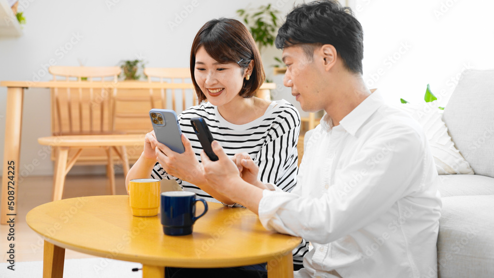 部屋でスマートフォンを操作する男性と女性 部屋でスマートフォンを操作する男性と女性