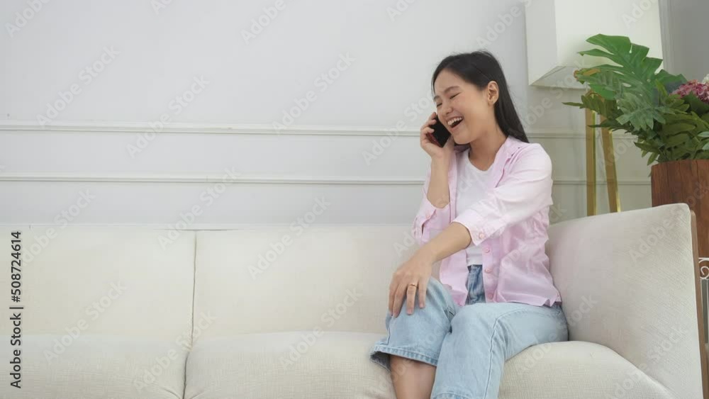 Happiness young asian woman sitting on sofa and talking with smartphone at home, female calling and speaking and listening with smart phone on couch at house, lifestyles and communication concept. Happiness young asian woman sitting on sofa and talking with smartphone at home, female calling and speaking and listening with smart phone on couch at house, lifestyles and communication concept.